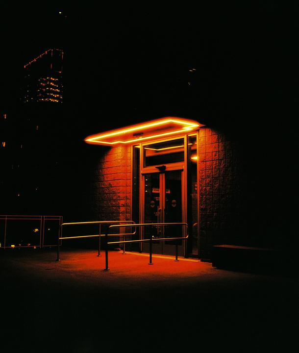 A building entrance with a neon light above it is illuminated at night.