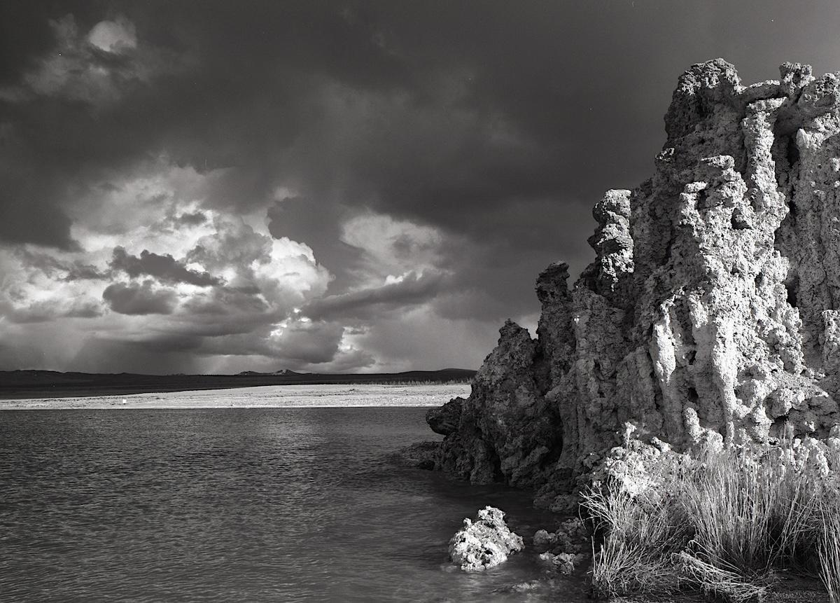 A body of water with tufa formations on the right and a cloudy sky above.