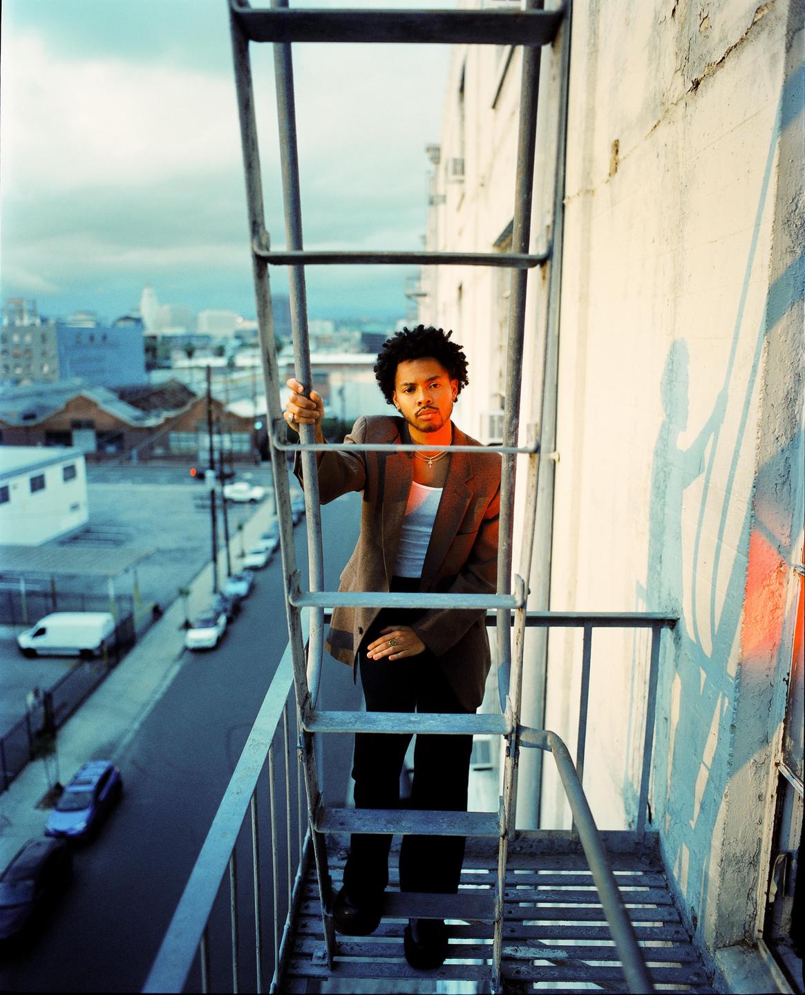 A man stands on a fire escape overlooking a city street.