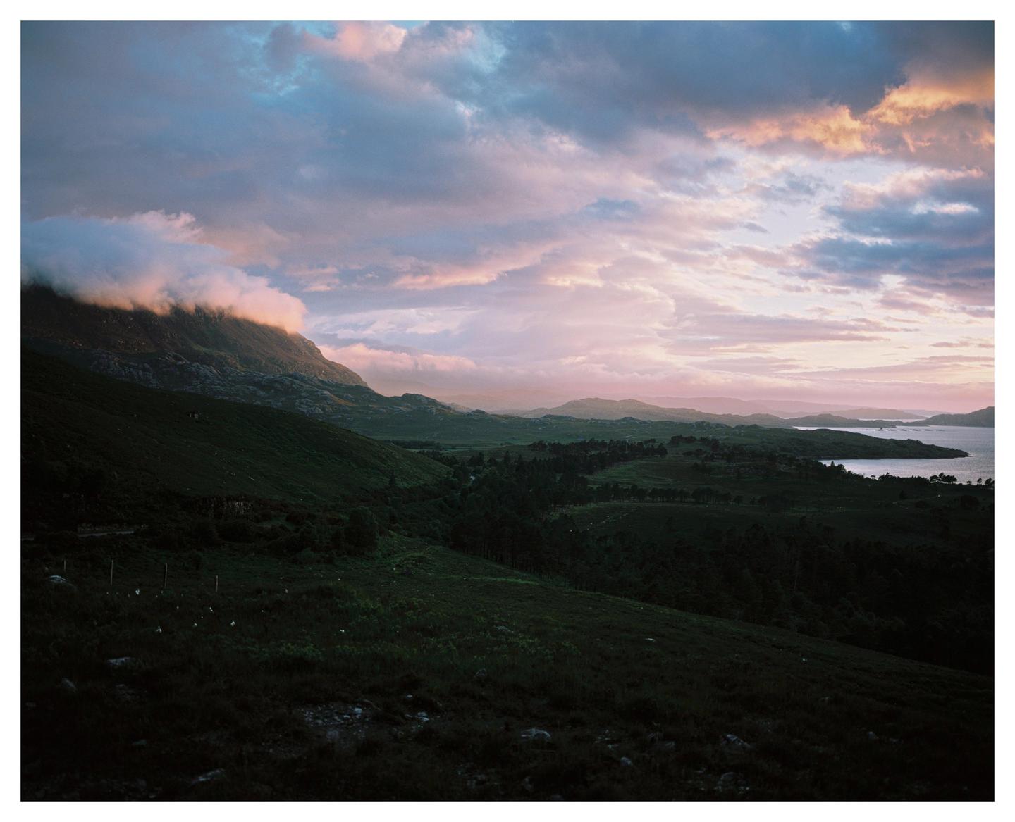 Clouds hang over a mountain and a body of water at sunset.
