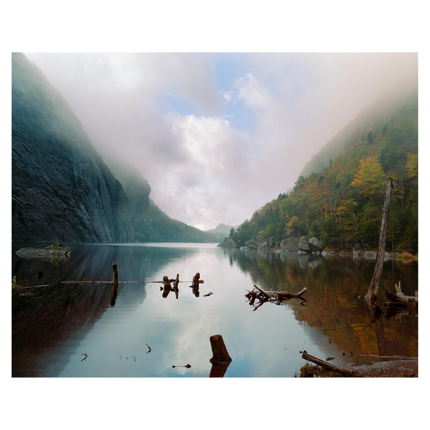 A lake is surrounded by mountains with autumn foliage and a cloudy sky.