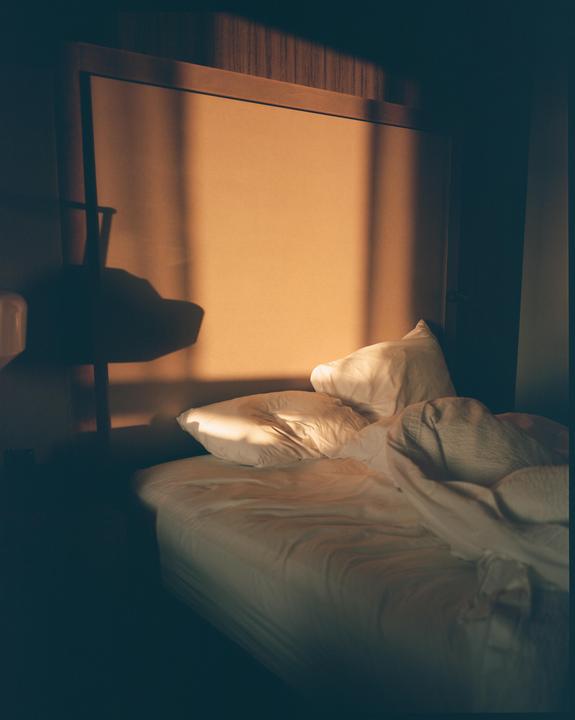 Sunlight casts a shadow on a bed with white sheets and pillows.