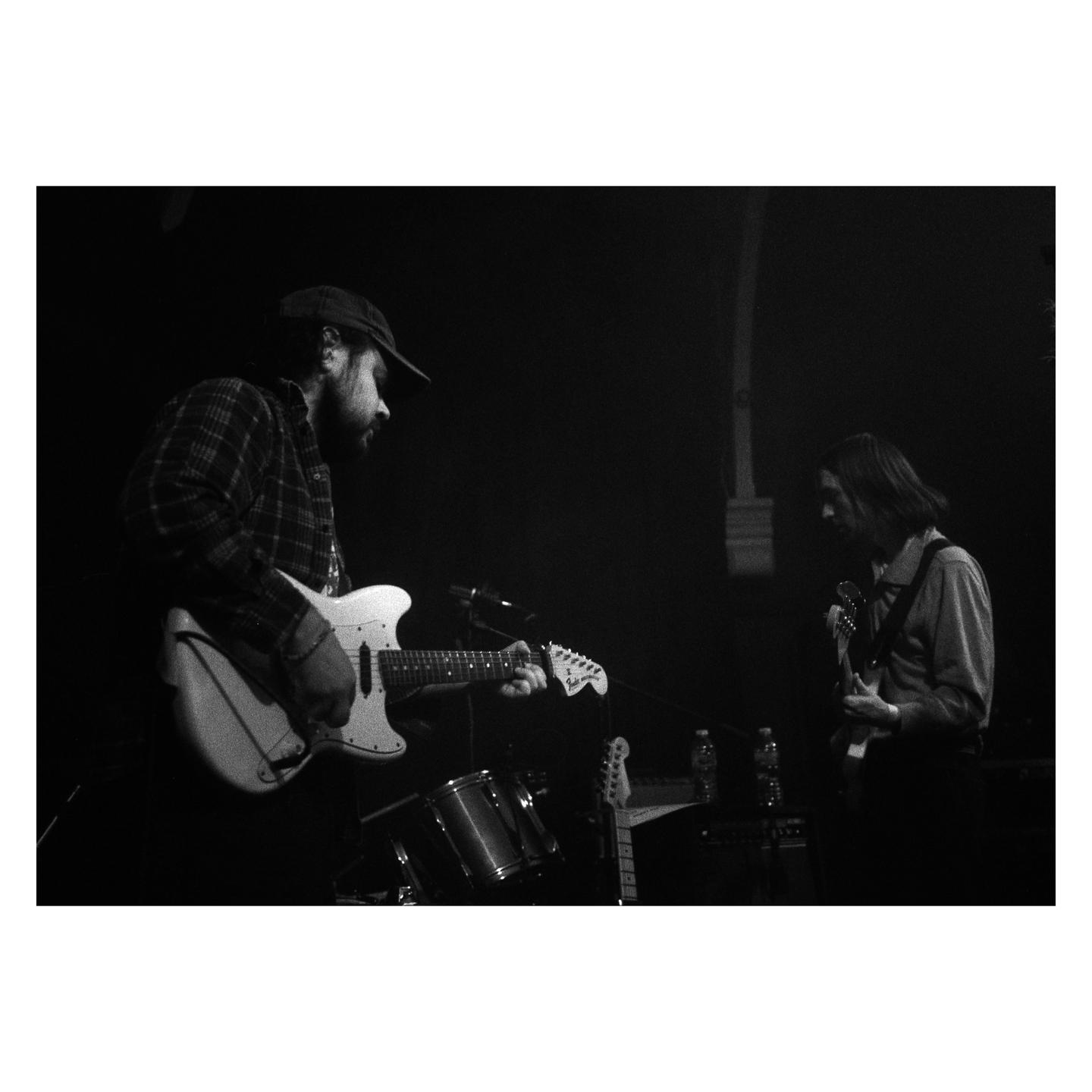 Two men play electric guitars on a dark stage.
