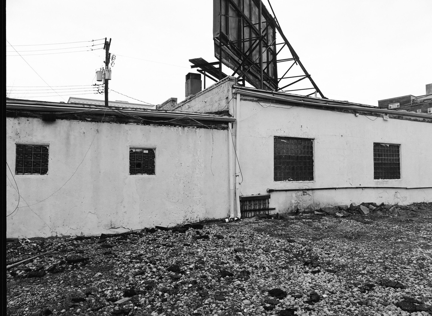 A white building with several windows and a large billboard on the roof stands next to a gravel lot.