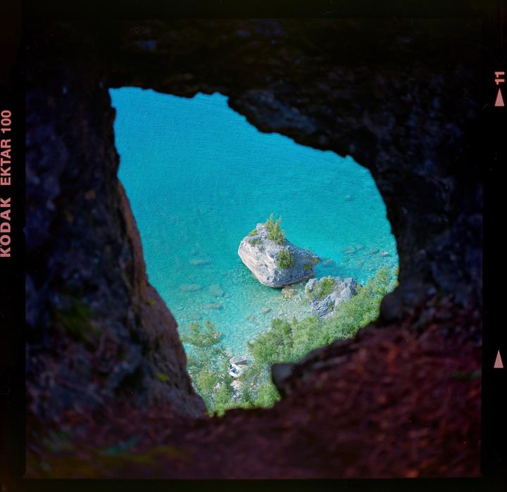 A view of a rocky island in turquoise water is framed by a dark cave opening.