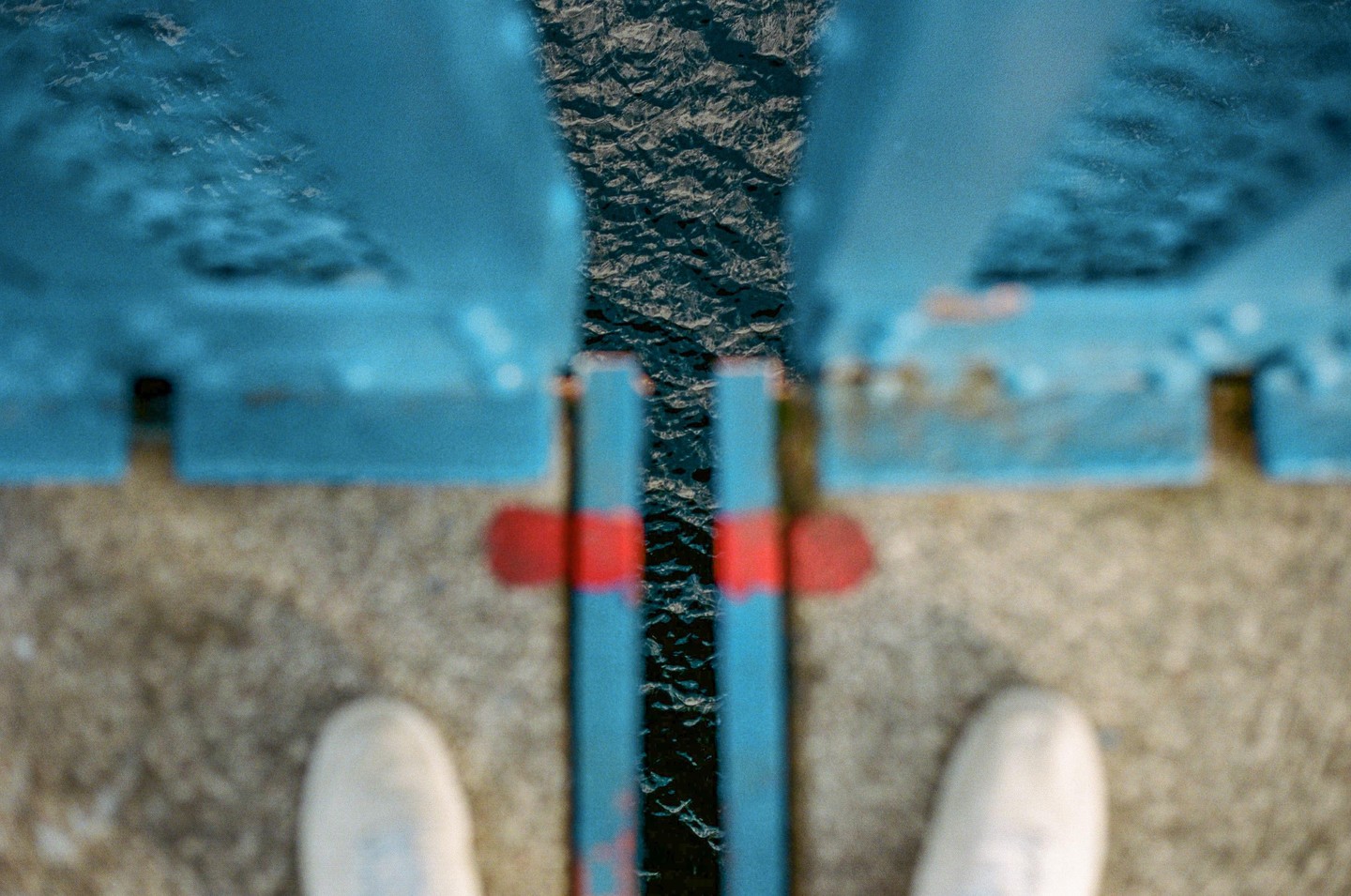 A person's feet stand on a bridge looking down at the water below.
