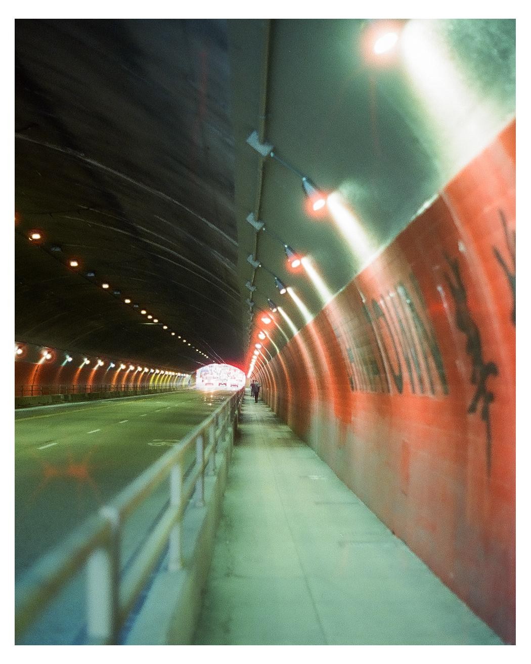 A person walks along a pedestrian path inside a brightly lit tunnel with a red wall.