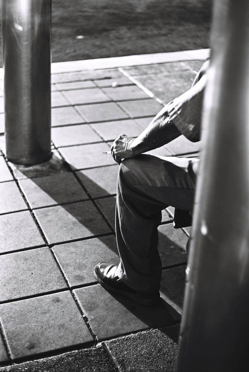 A person sits on a tiled surface, holding a cigarette between their fingers.