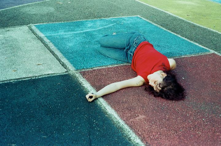 A woman in a red shirt and jeans lies on a colorful paved surface.