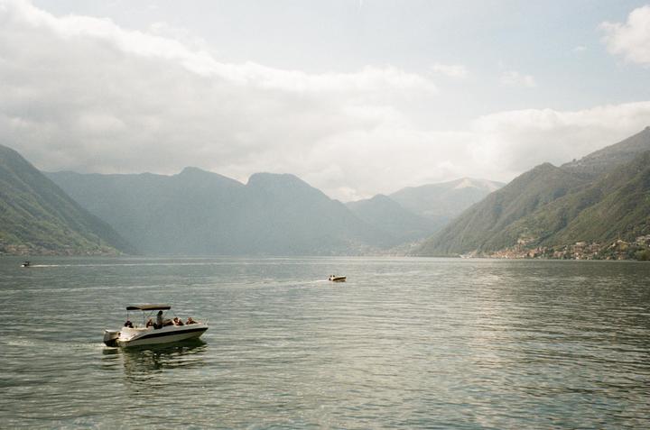 A motorboat with people on board cruises on a lake surrounded by mountains under a cloudy sky.