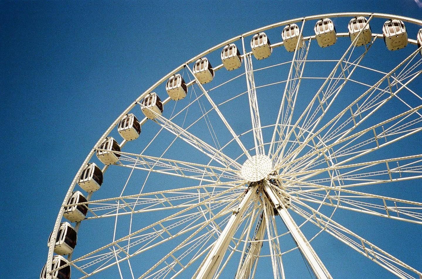 A white ferris wheel with many gondolas is set against a clear blue sky.