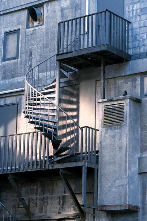 A spiral staircase with a small balcony is attached to the side of a concrete building.
