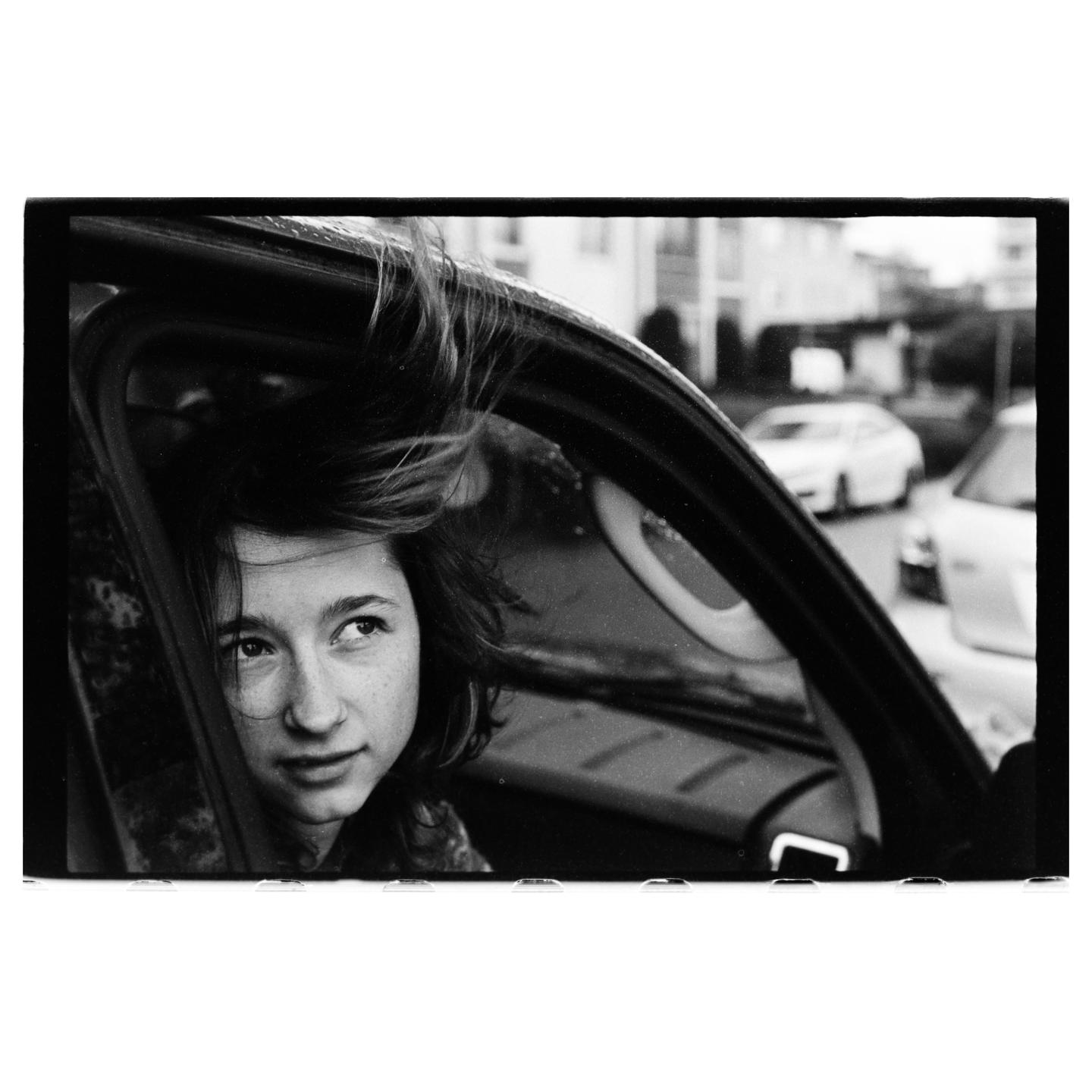 A girl with windblown hair looks out of a car window.