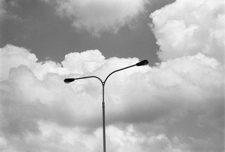 A street light with two lamps stands against a cloudy sky.