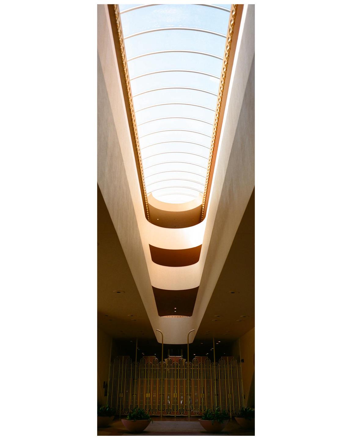 A long, narrow skylight illuminates the interior of a building with a golden gate at the bottom.