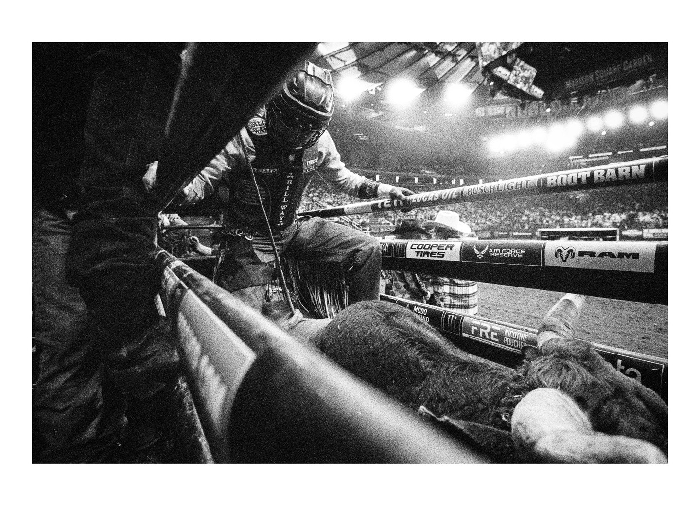A cowboy in a helmet and protective gear prepares to ride a bull in an arena.