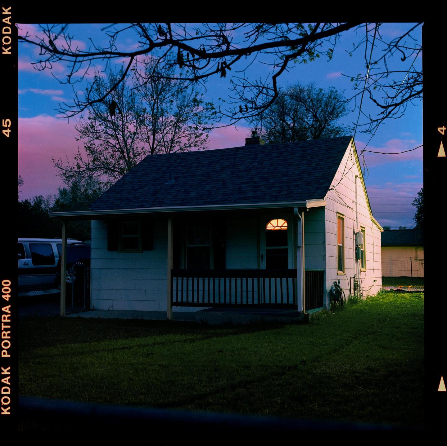 A small house with a porch is illuminated by a single light at dusk.