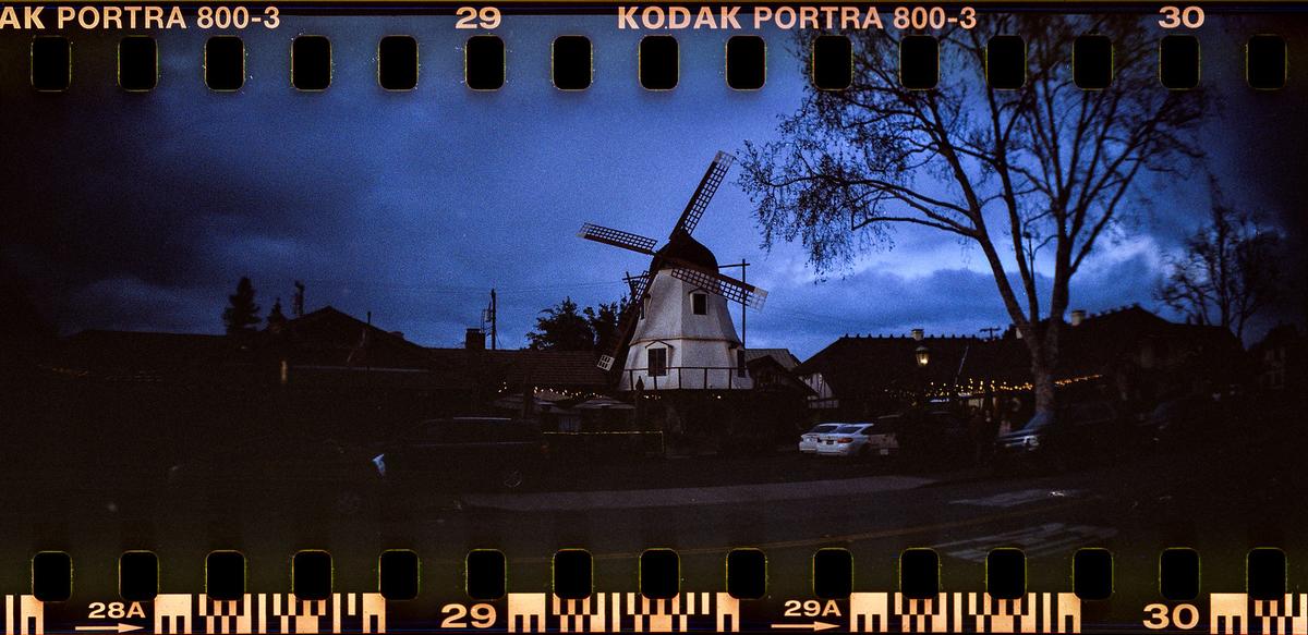A white windmill stands under a dark blue sky with bare trees and buildings in the background.