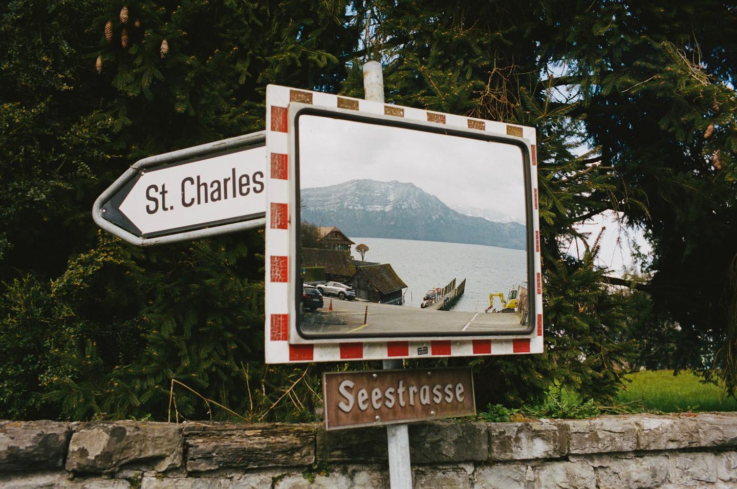 A street sign for St. Charles and a mirror reflecting a lake with mountains in the background are visible through pine branches.