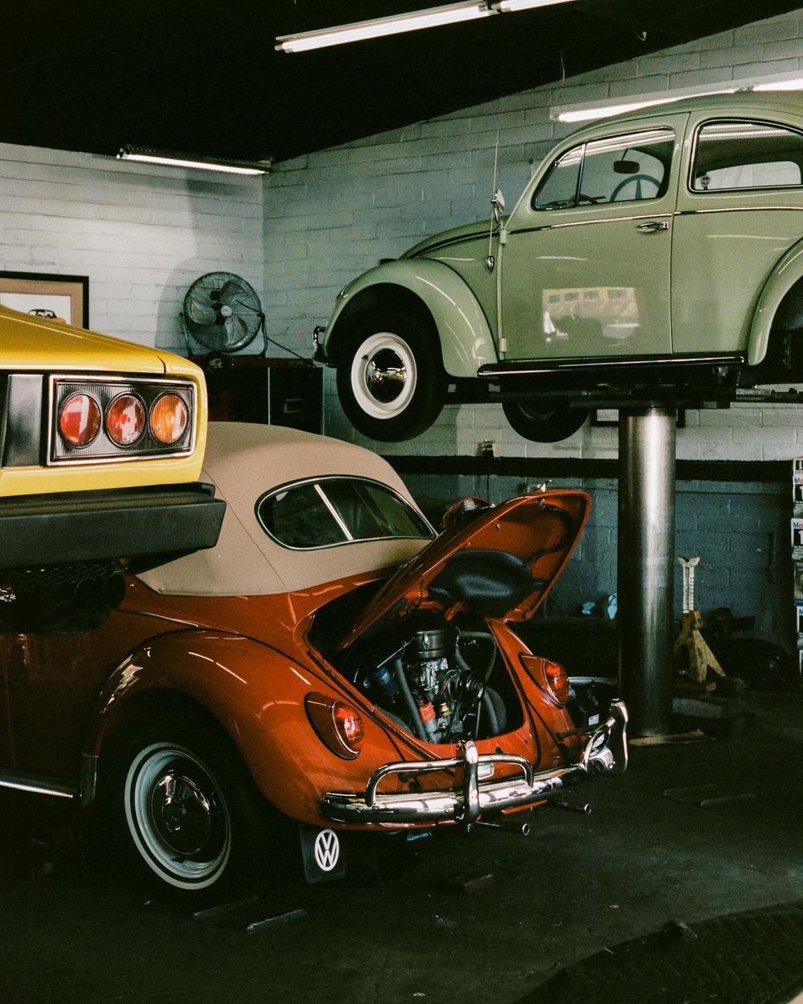 Three vintage cars are parked inside a garage, with one car elevated on a lift.