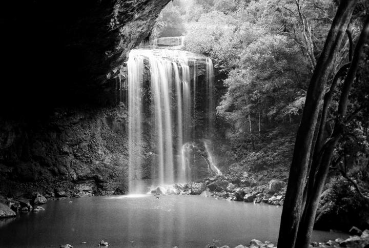 A waterfall cascades into a pool surrounded by rocks and trees.