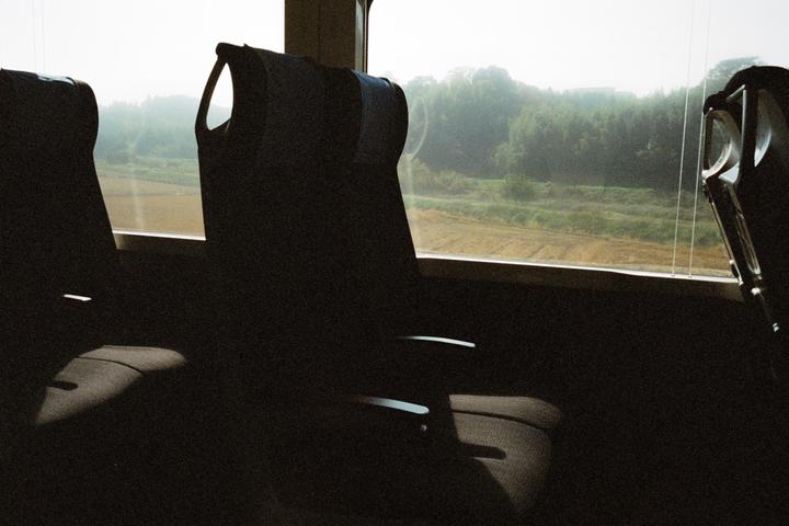 The interior of a train car is visible with three seats and a window looking out onto a rural landscape.