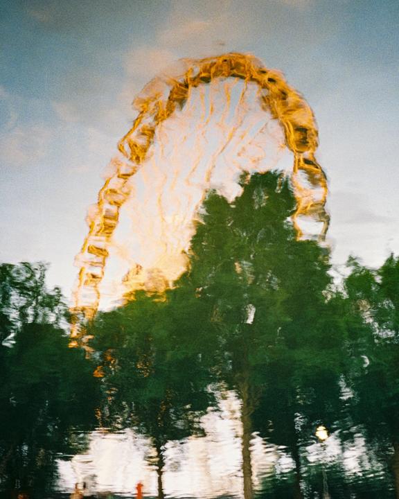 A distorted reflection of a ferris wheel and trees is visible in water.