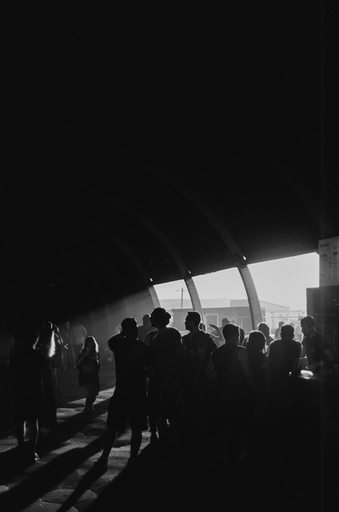 A group of people are silhouetted against a bright light source in a dark, arched structure.