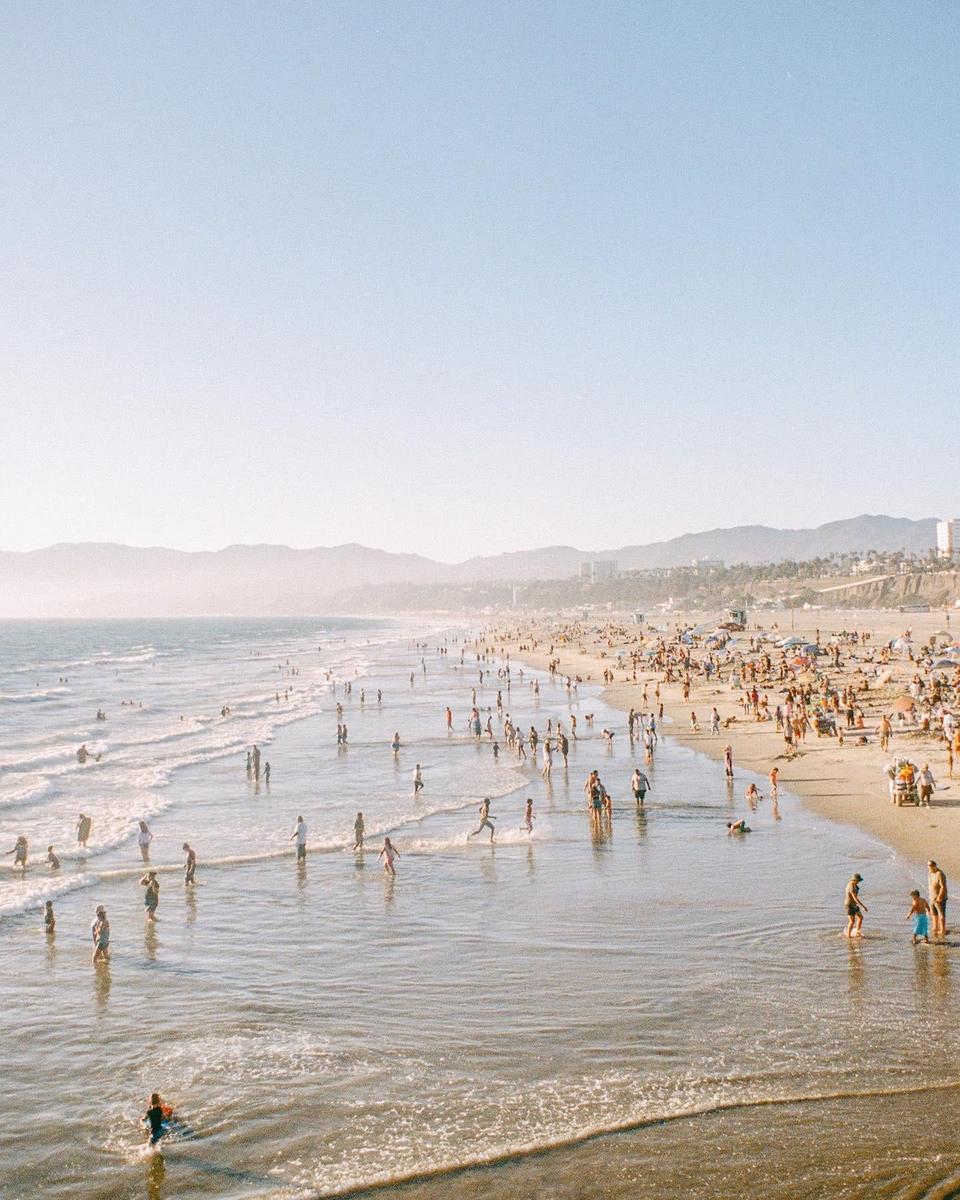 A crowded beach with many people in the water and on the sand is visible under a hazy sky.