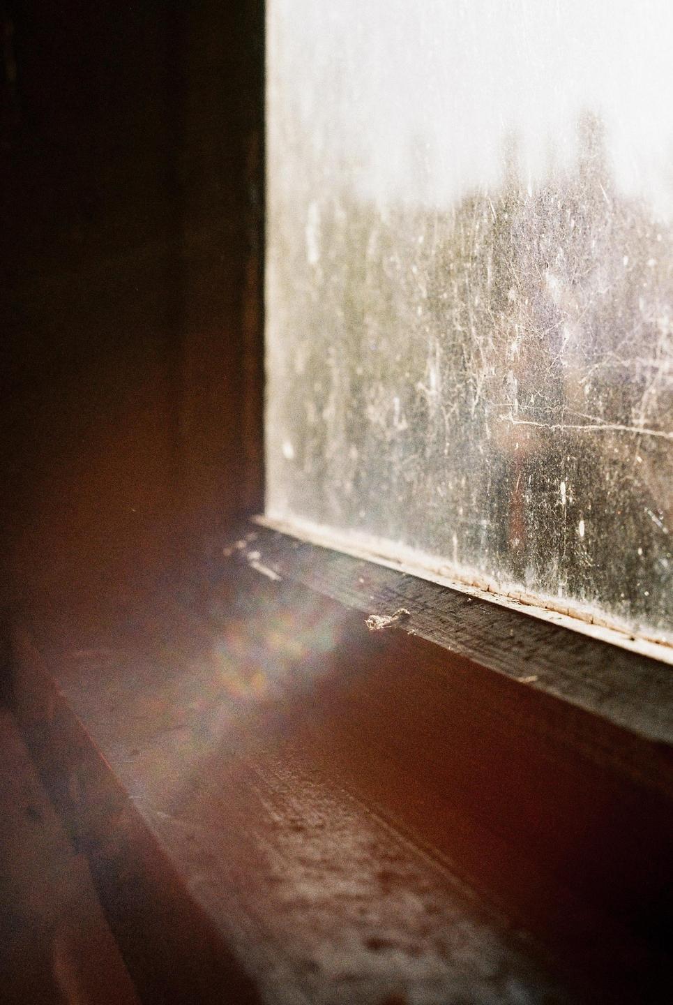 A dirty window and wooden window sill are illuminated by sunlight.
