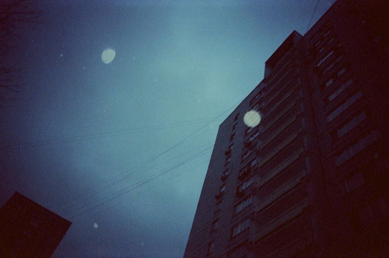 A tall building stands against a dark blue sky with visible power lines and light flares.