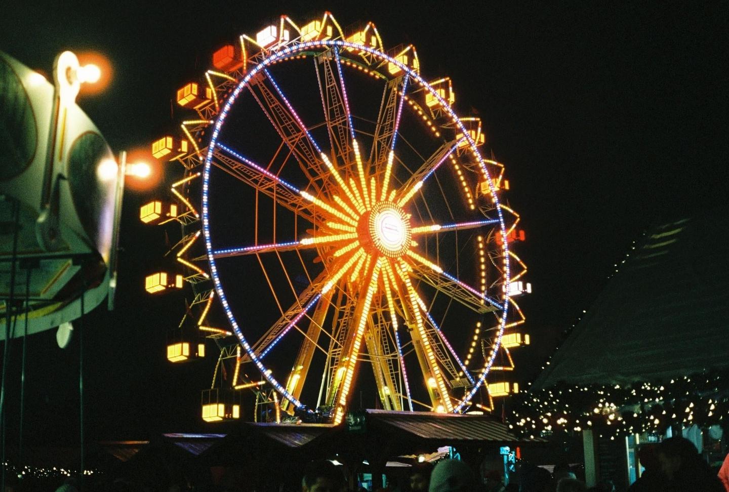 A brightly lit ferris wheel stands out against the dark night sky at a Christmas market.