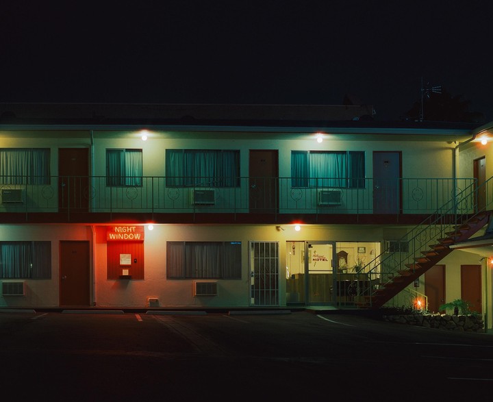 A two-story motel with a neon "Night Window" sign is illuminated at night.