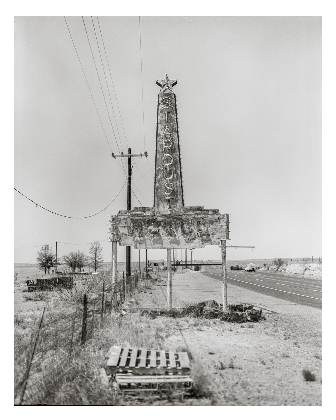 A tall, weathered sign for "Stardust" with a star on top stands beside a road in a dry, rural landscape.