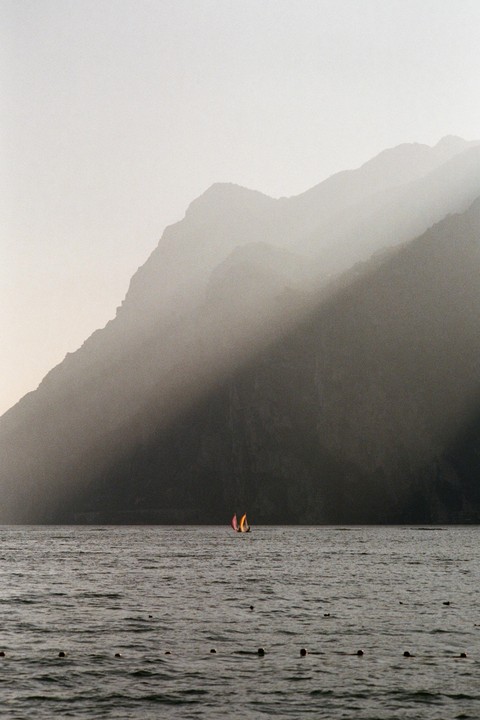 Two small sailboats with colorful sails are on a lake with mountains in the background.