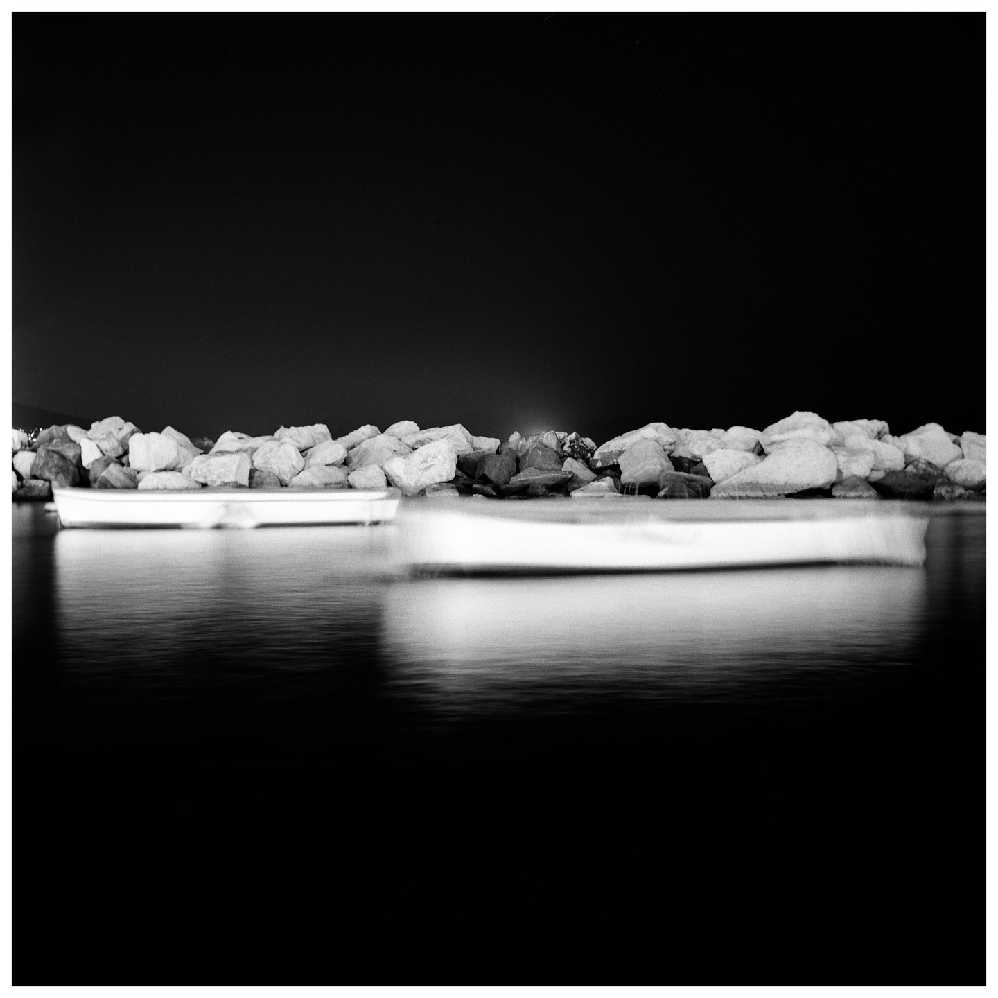 Two boats are on the water next to a rocky shore at night.