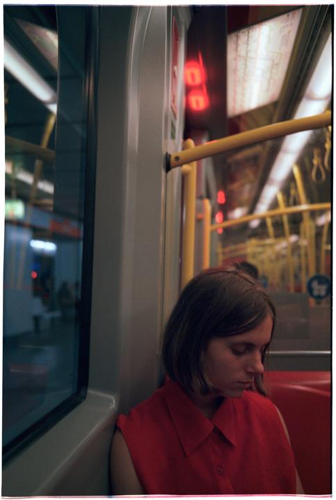 A woman in a red shirt sits on a train next to a window at night.