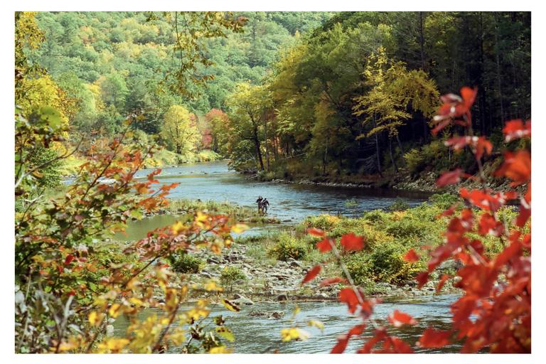 Two fishermen stand in a river surrounded by autumn foliage.