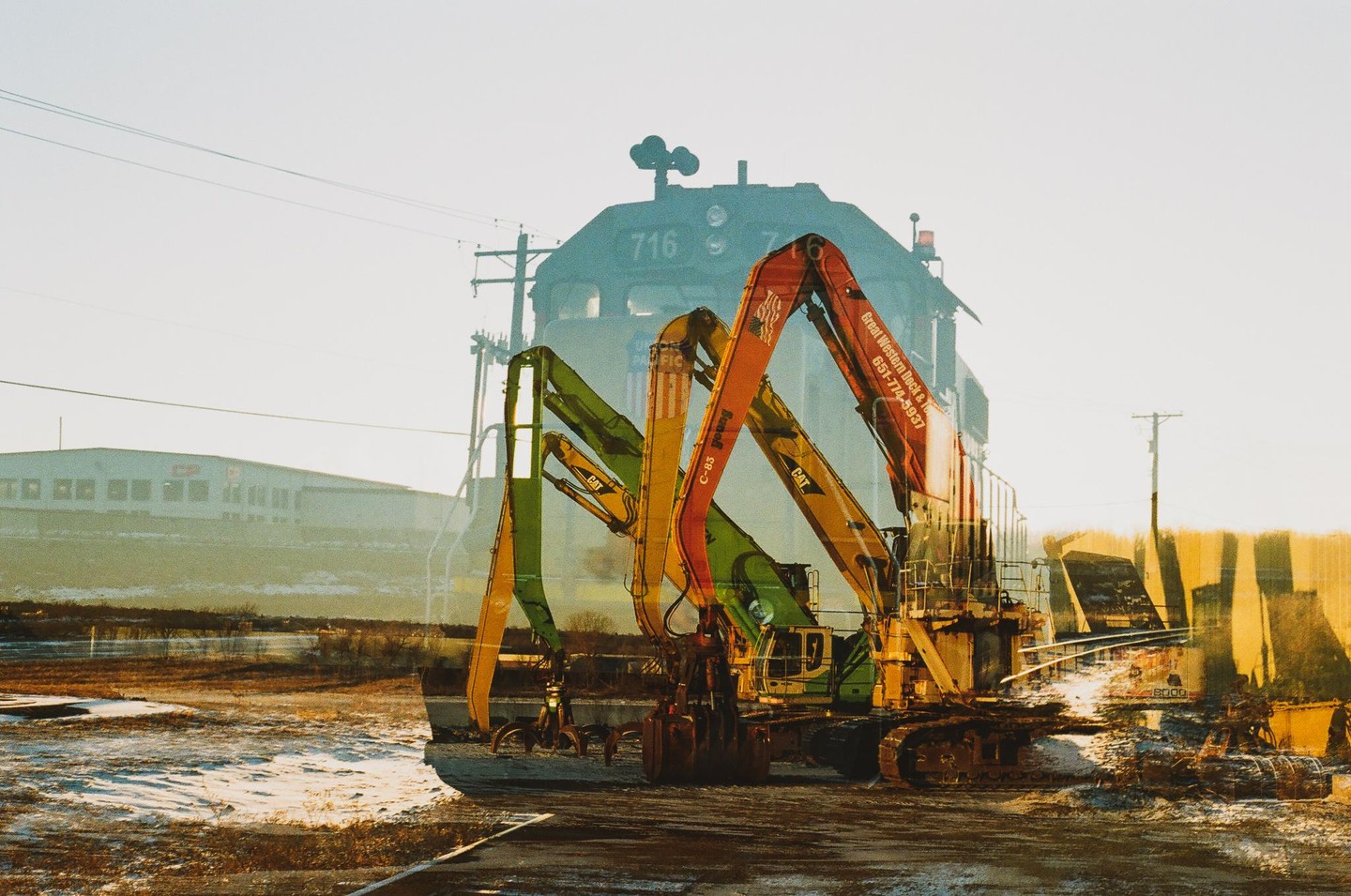 A double exposure shows a train and several excavators in an industrial setting.