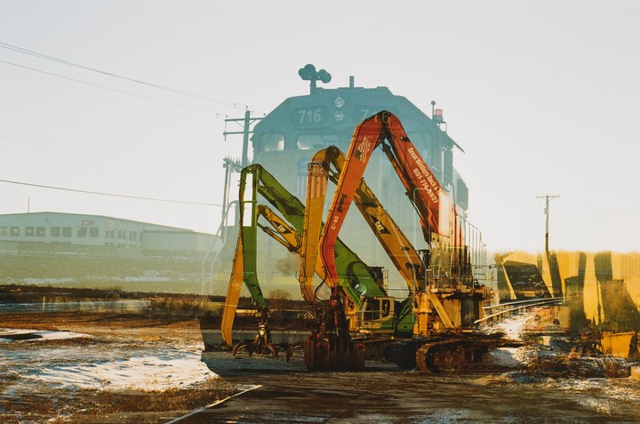 A double exposure shows a train and several excavators in an industrial setting.