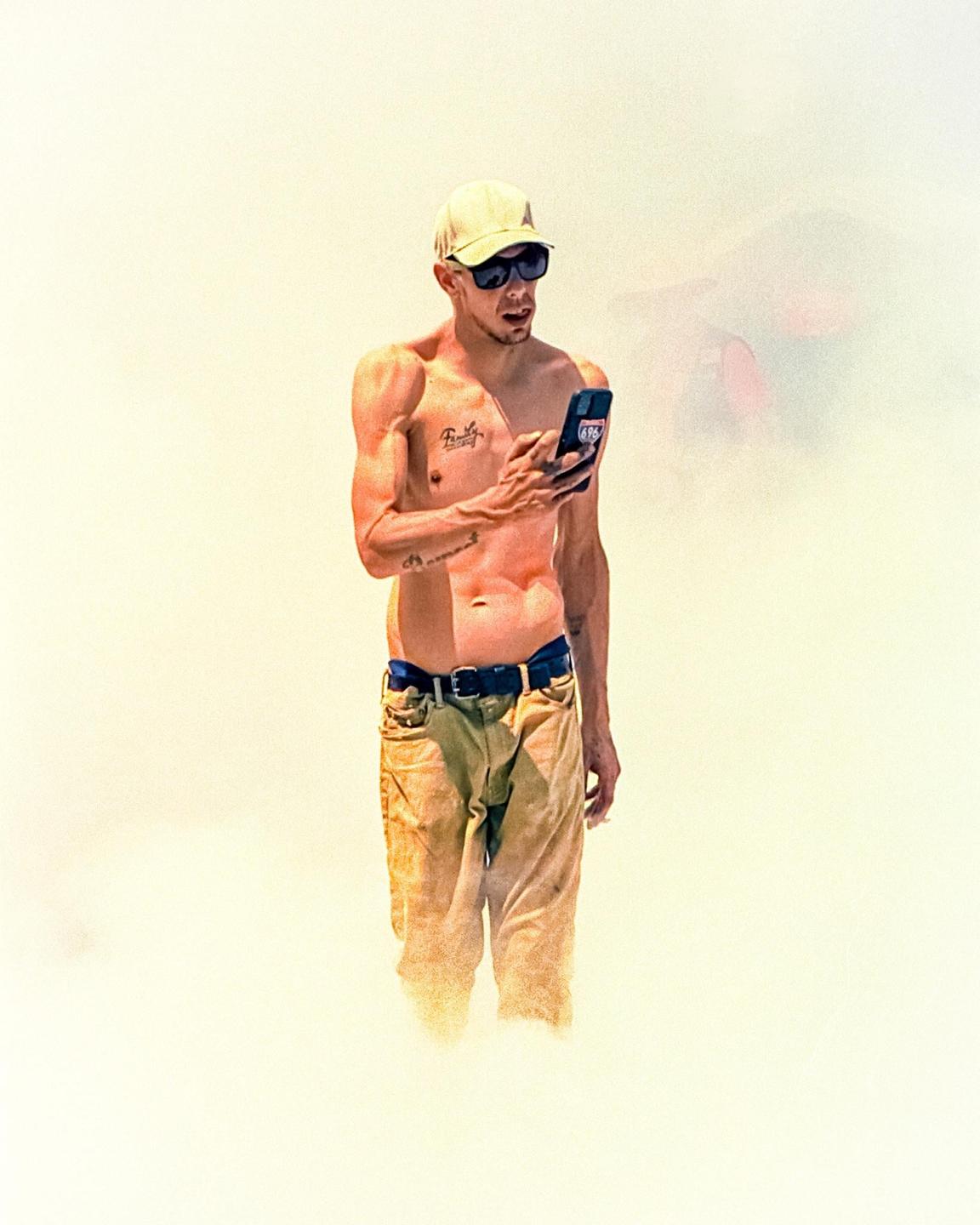 A man wearing a cap and sunglasses is looking at his phone.