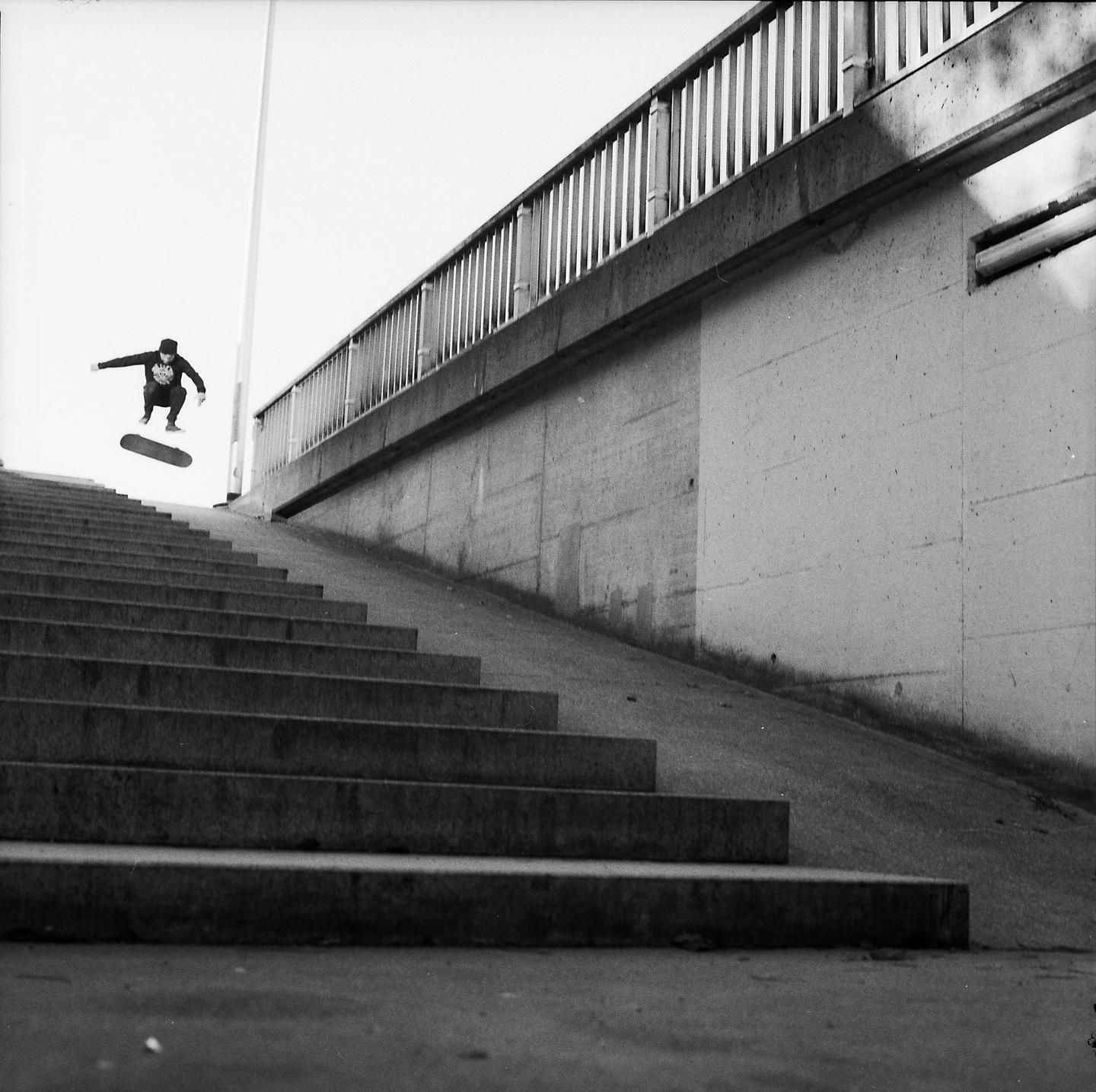 A skateboarder jumps in the air next to a concrete wall and stairs.