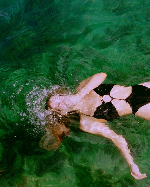 A woman floats on her back in green water, with bubbles around her head.