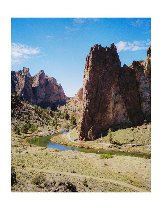 A winding river flows through a valley surrounded by towering rock formations under a bright blue sky.
