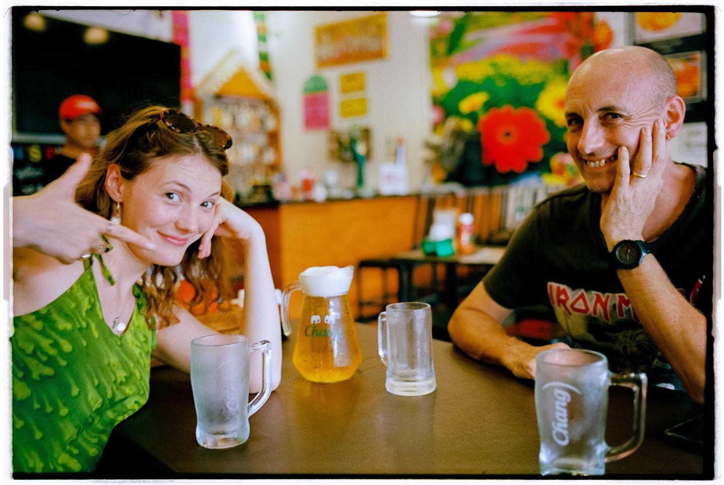 A woman and a man sit at a table with drinks in a colorful restaurant.
