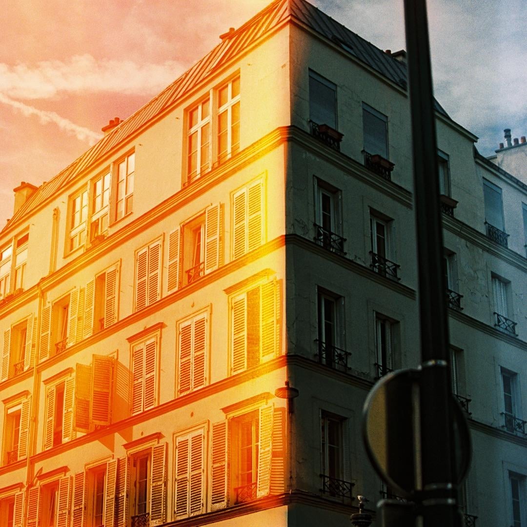A building with many windows and shutters is illuminated by a strong light leak on its left side, while the right side is in shadow.