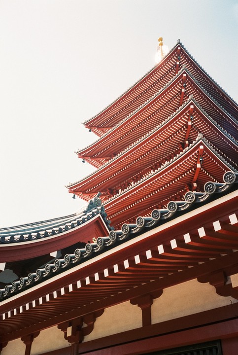 A red pagoda with multiple tiers and a white sky is seen from a low angle.