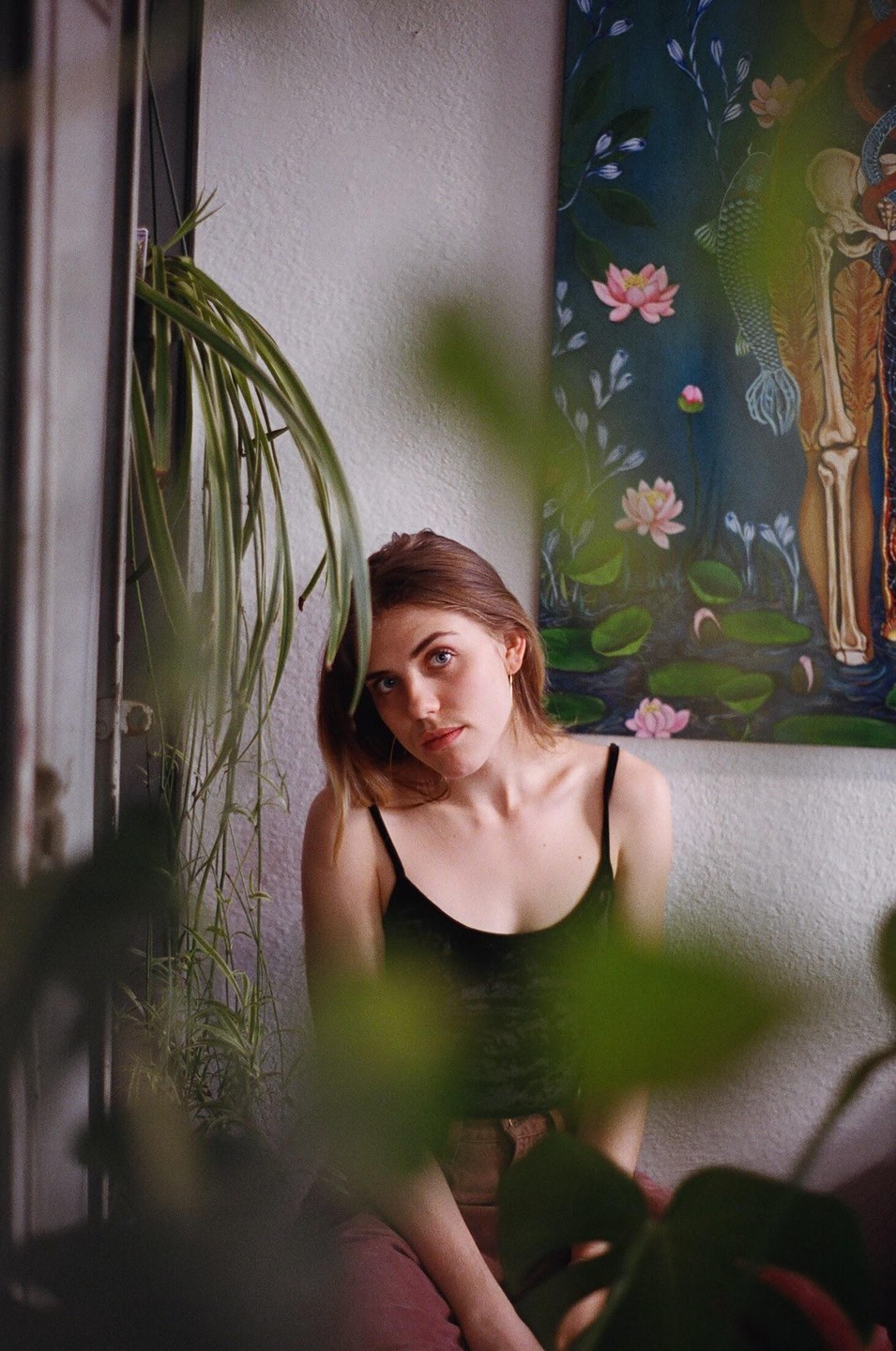 A woman with brown hair and a black top sits in front of a painting of water lilies and a human skeleton.