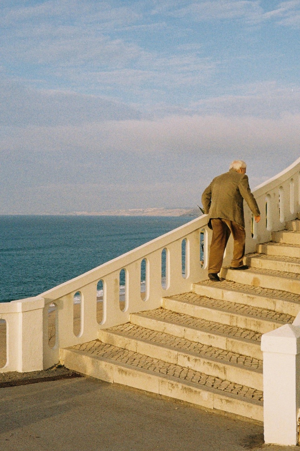An older man walks up a set of outdoor stairs next to the ocean.