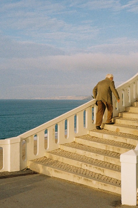 An older man walks up a set of outdoor stairs next to the ocean.